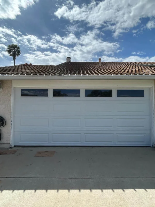 White long-panel sectional garage door with top windows installed under a tile roof
